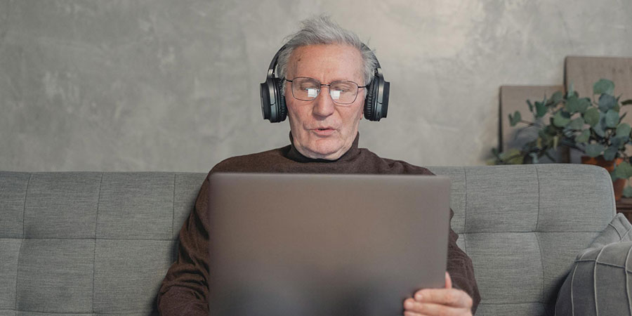 elderly man wearing headphones and using a laptop while sitting on a couch