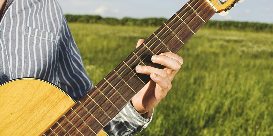 a person playing an acoustic guitar in a green grass field